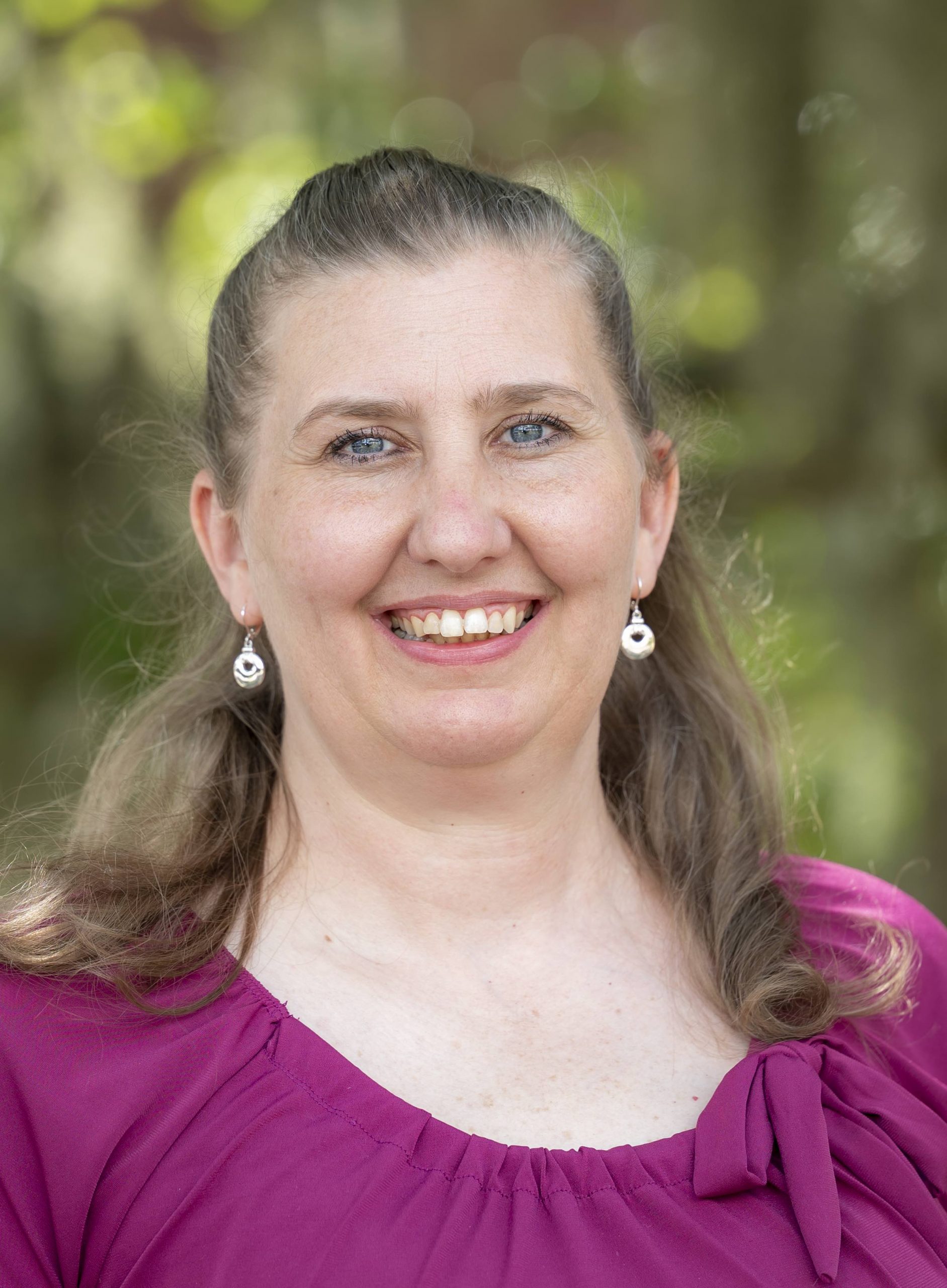 Person smiling in front of trees. 