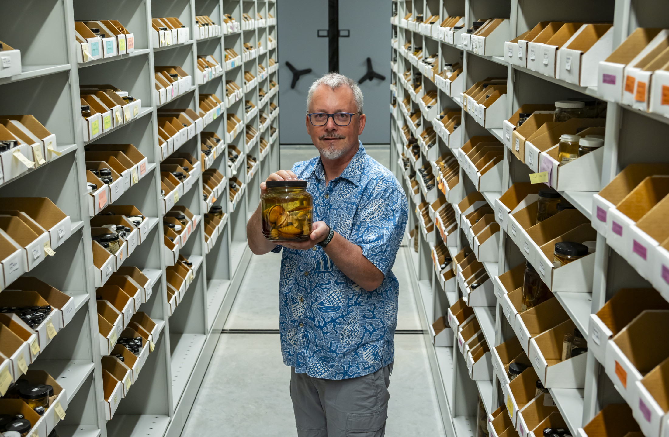 John Slapcinsky stands in the museum's invertebrate zoology collection, holding a jar.