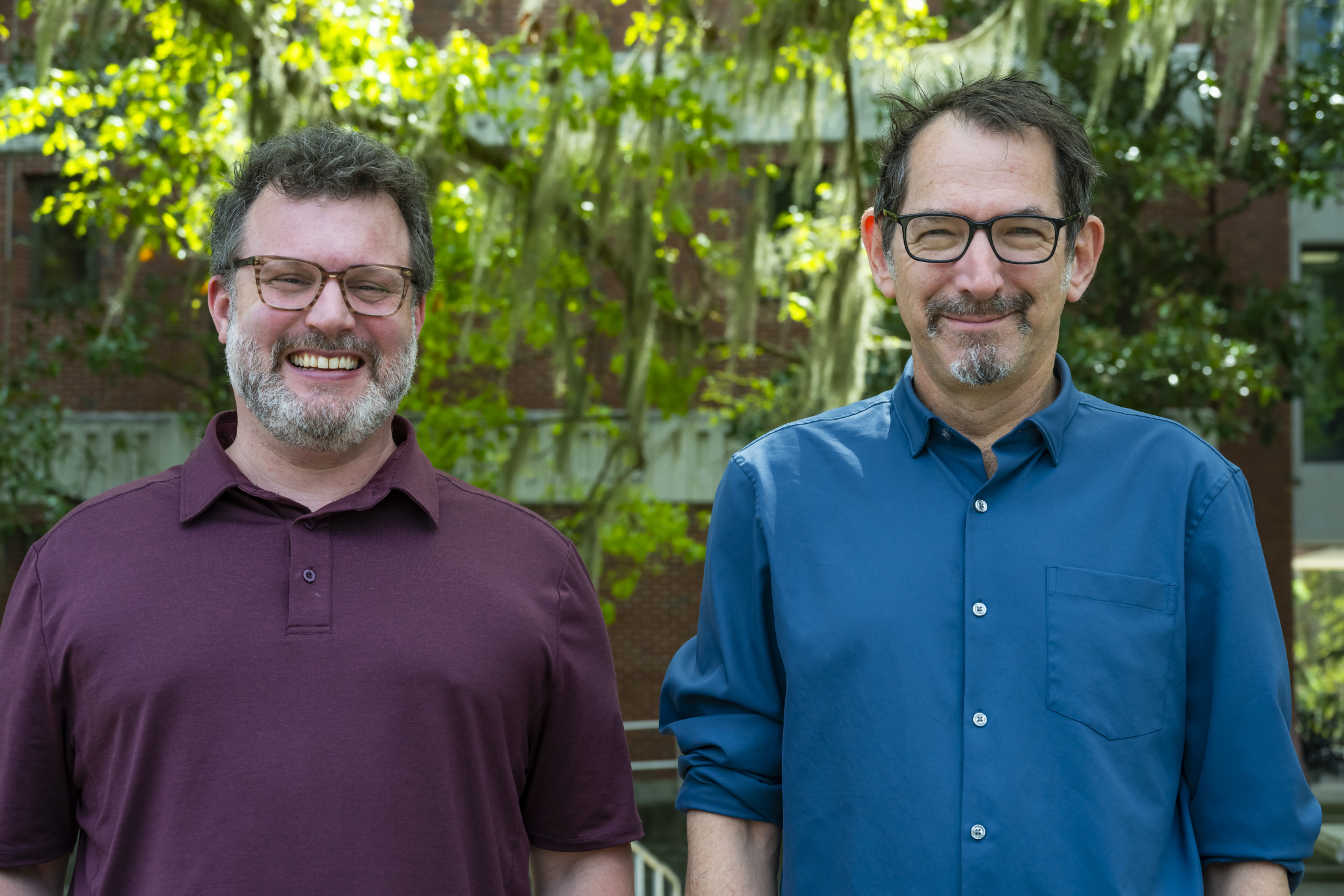 Two people stand side by side in front of tree branches.