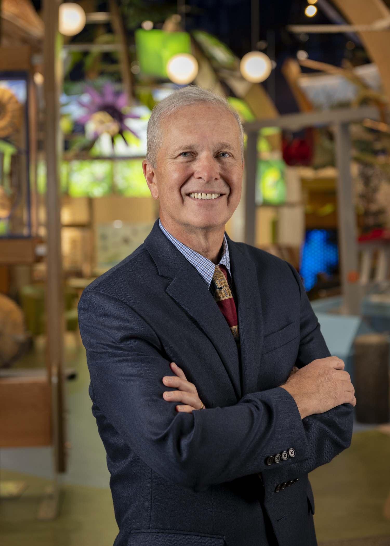 Man in a suit smiles while standing in front of a museum exhibit.