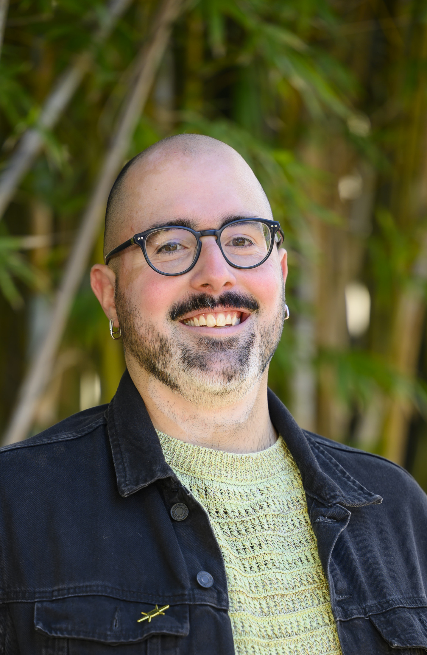 Person smiles in front of a bamboo hedge.