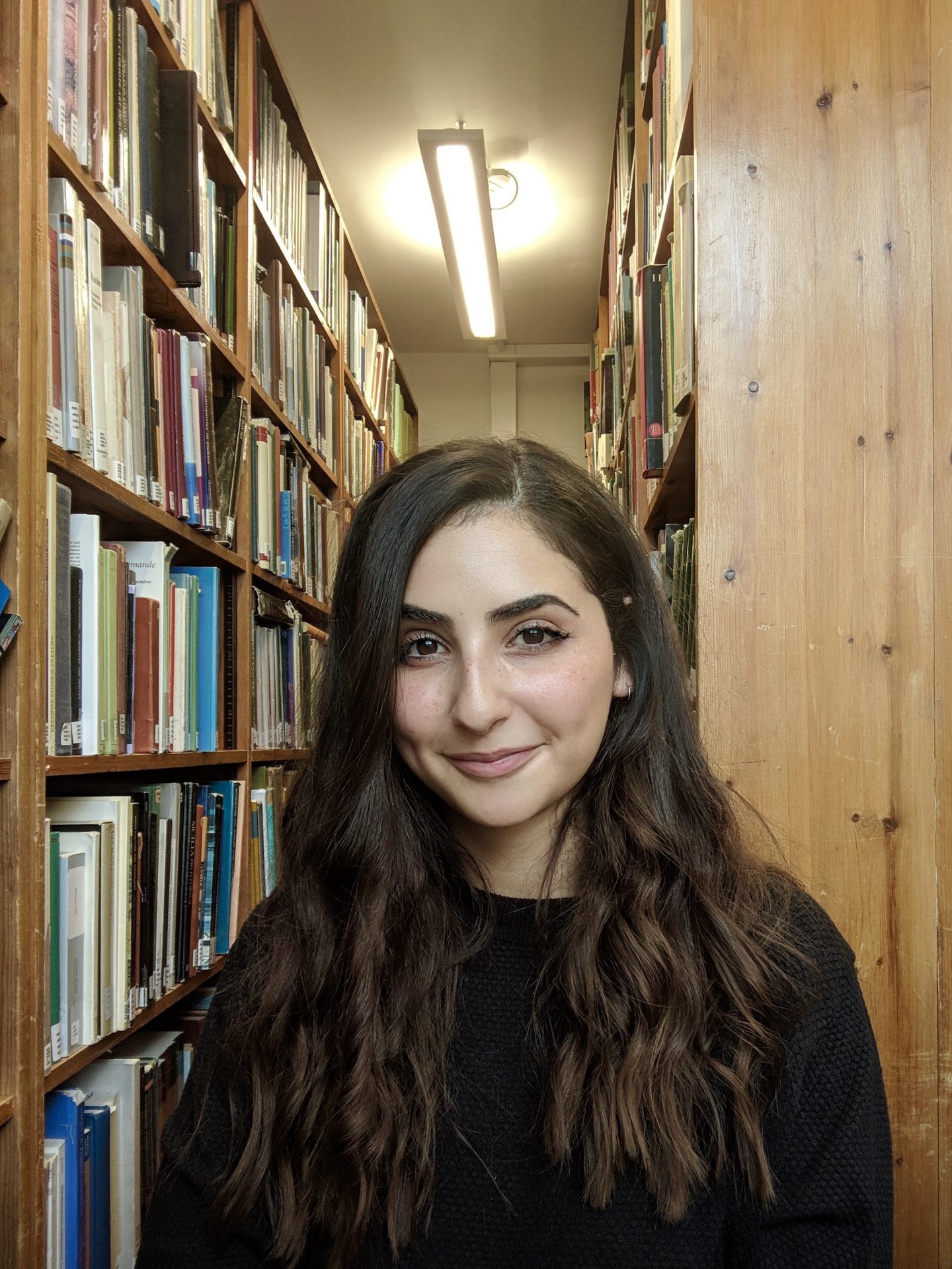Person standing in front of library stacks smiling for the camera. 