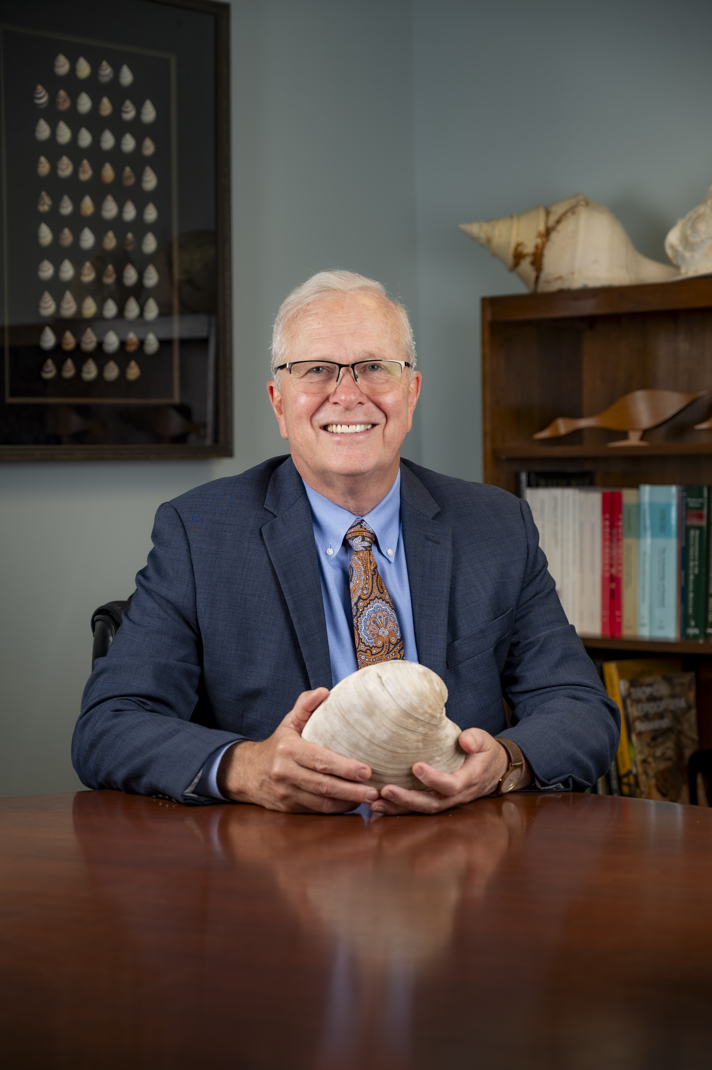 Person sitting at desk and holding a large shell smiles for the camera. 