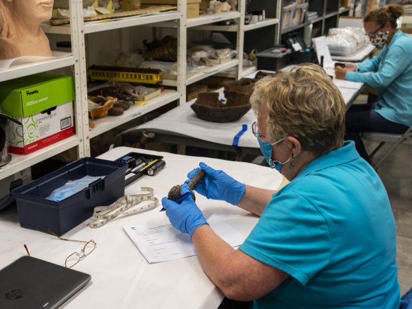 Person inspecting an artifact while wearing gloves and sitting at a desk.