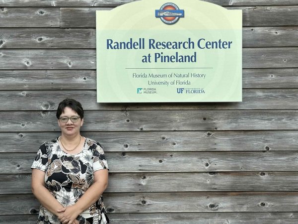 Person stands in front of a wooden, plank wall next to a sign that says "Randell Research Center at Pineland."