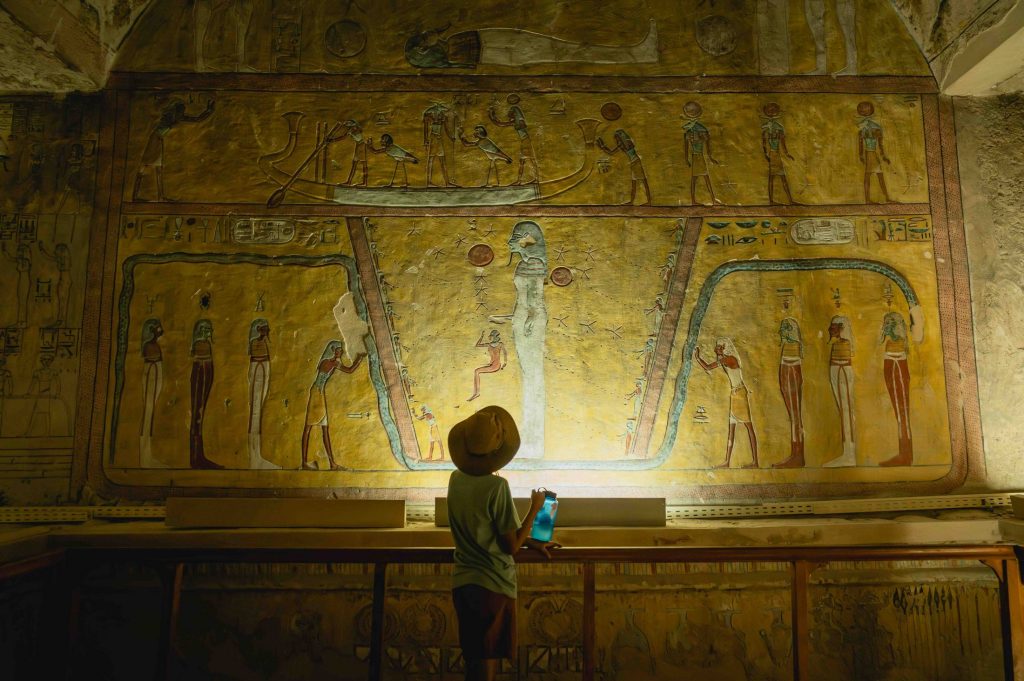 Child looks up at illuminated hieroglyphics in Egyptian tomb.