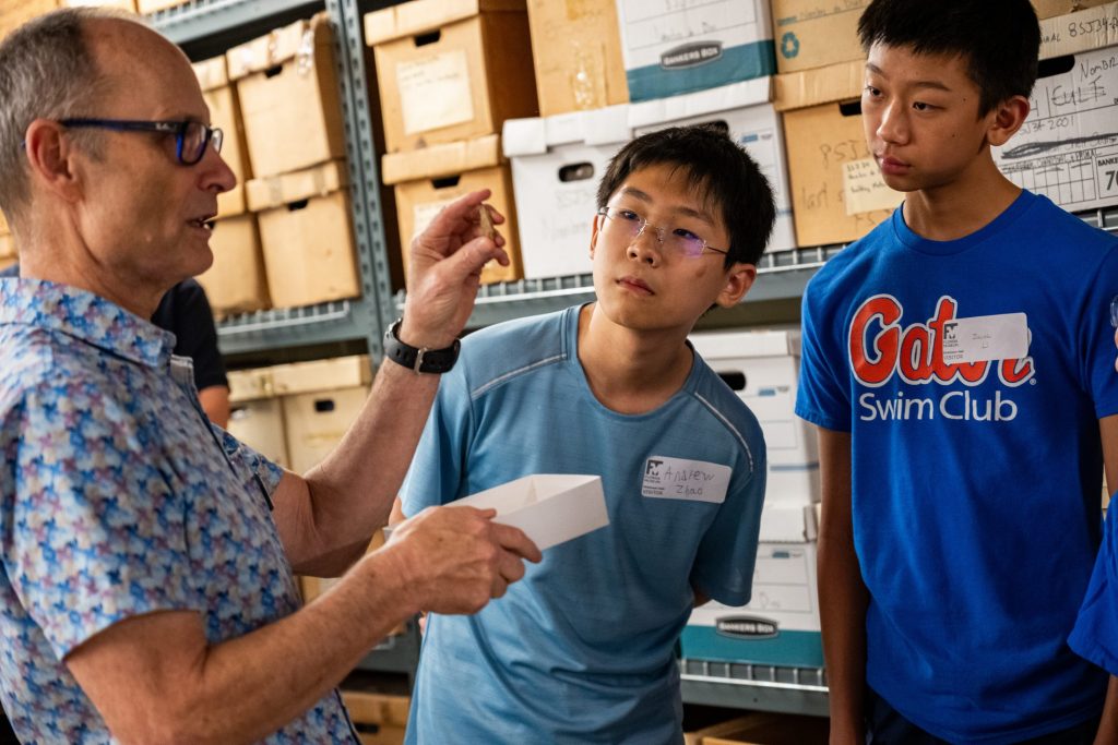 Photograph of a person holding up a small artifact while two kids look at it.