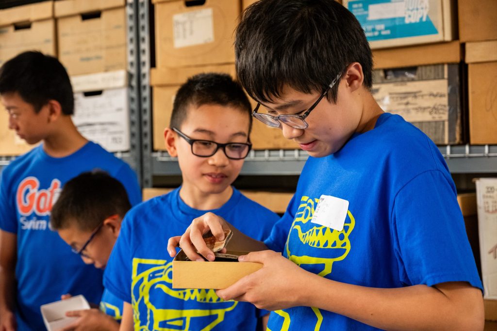 Photograph of a kid picking an artifact out of a box while another kid looks on.