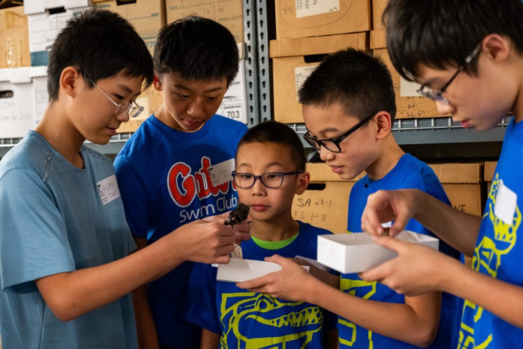 Photograph of five kids standing together and looking at an small artifact held by one of the kids.