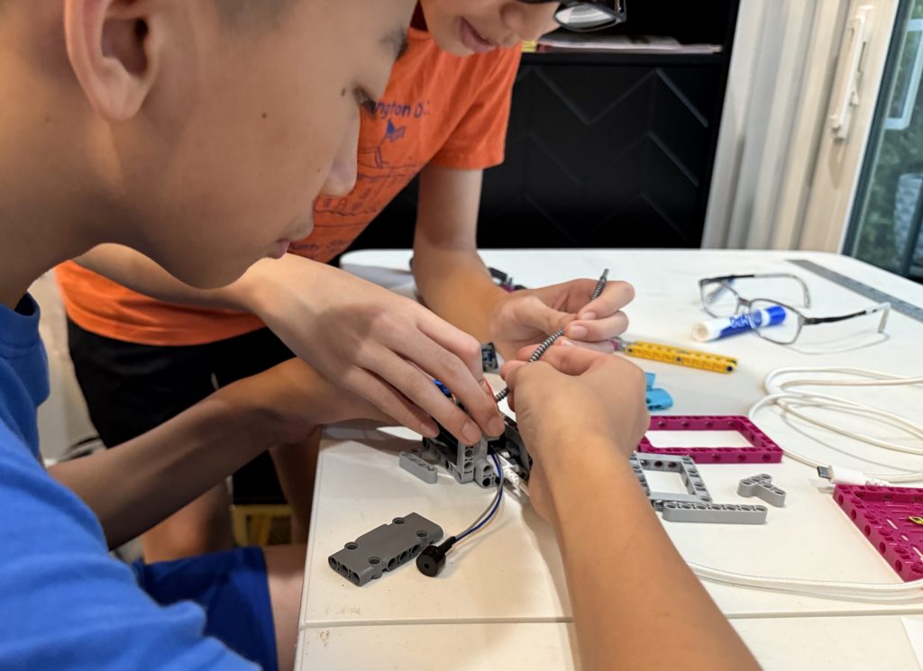 Photograph with a close-up view of the hands of two kids working on a Lego robot.