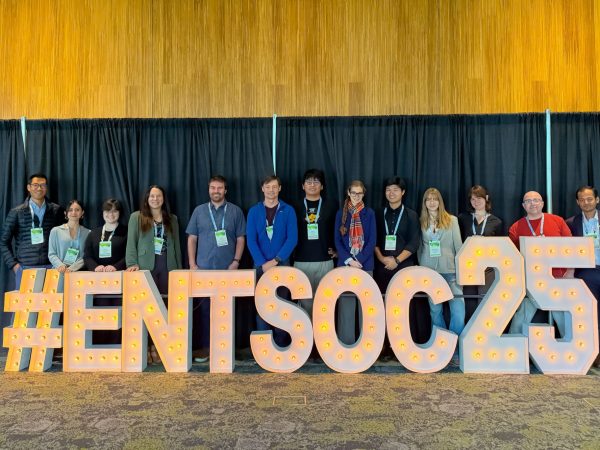 A group of people stand behind a lighted sign that reads "#ENTSOC25"