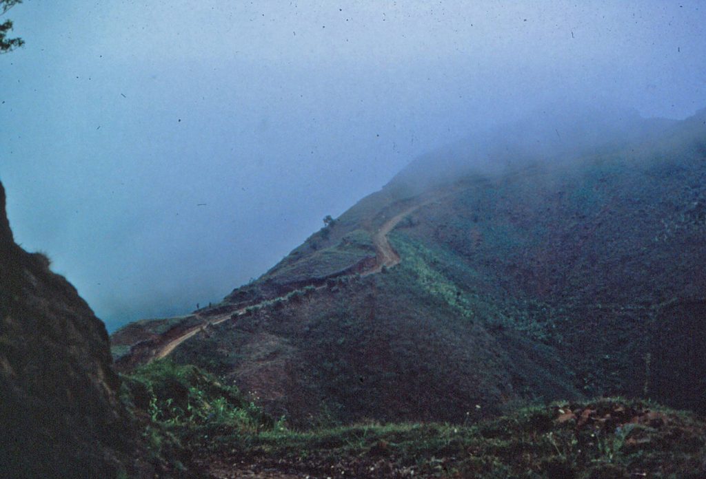 Photo of a dirt road going up a foggy mountain.