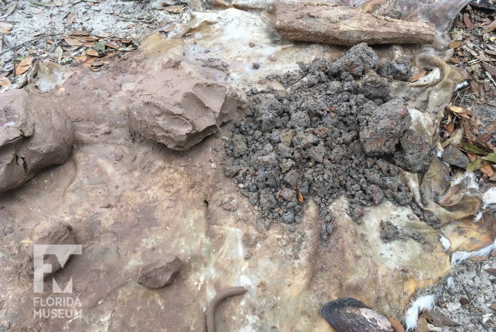 A deerhide with lump on pinkish clay on left, and mound of grayish lumps on the right