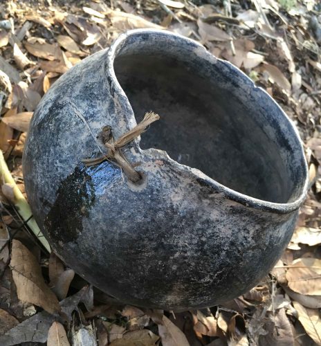 pot sitting on leaves with visible holes lashed with twine closing a crack.