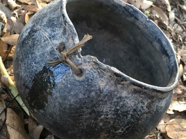 pot sitting on leaves with visible holes lashed with twine closing a crack.