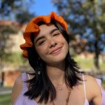 woman with dark hair wearing an orange hat, sitting outside