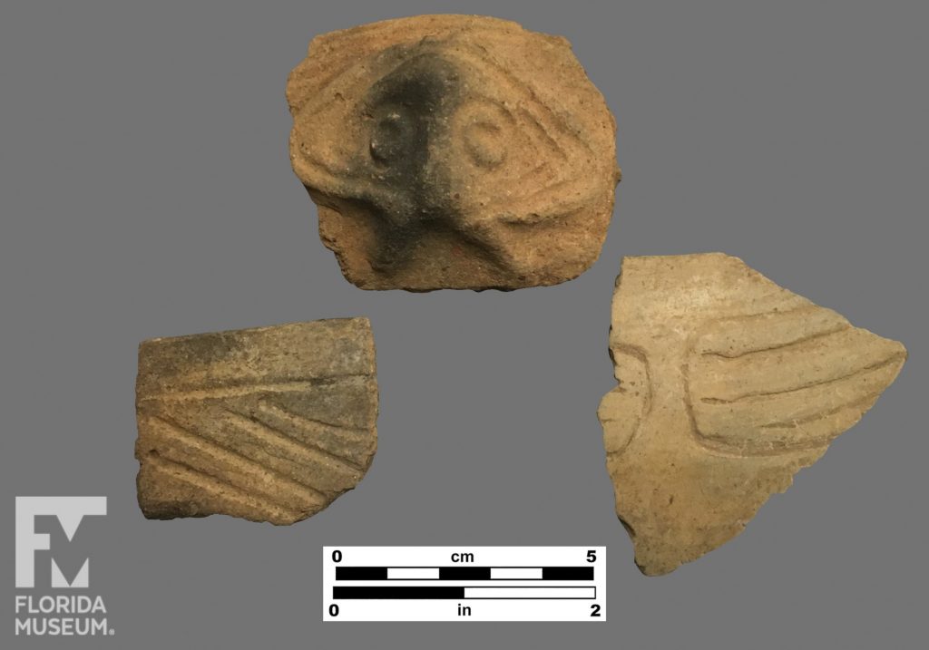 Formal artifact photo of three Chicoid sherds. The bottom left sherd has one horizontal incised line beneath the rim, and diagonal incizing along its body. The top sherd is an incised face adorno. The bottom left sherd is incised into a rectangular lozenge with parallel horizontal lines inside.
