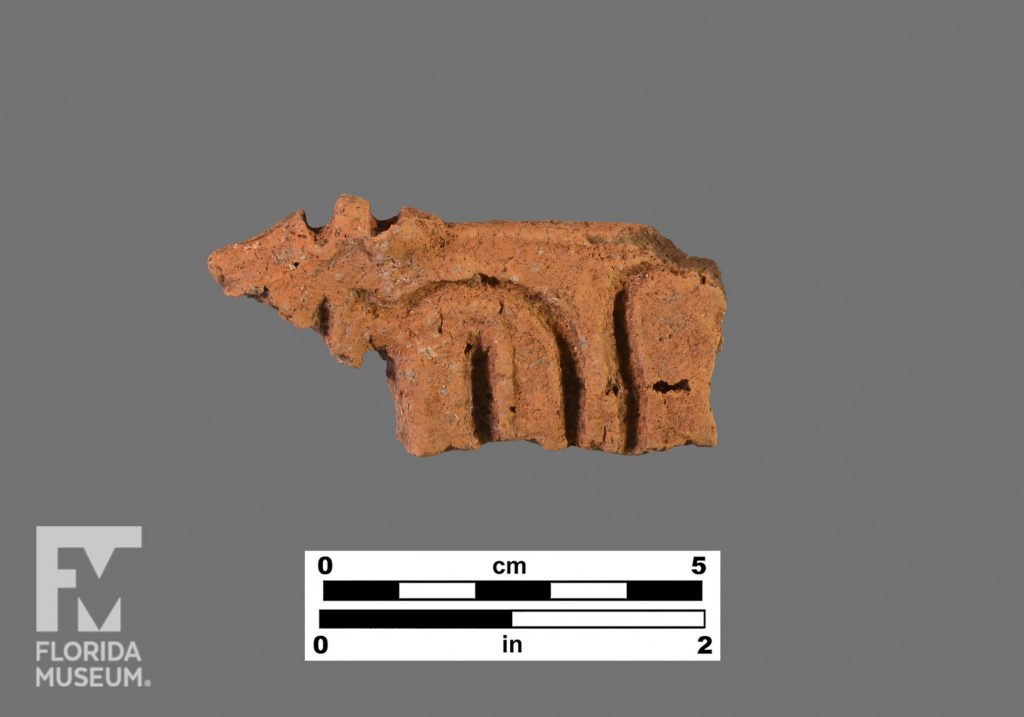 Formal artifact photo of a ceramic sherd with a modeled triangular end piece and incising along its body.