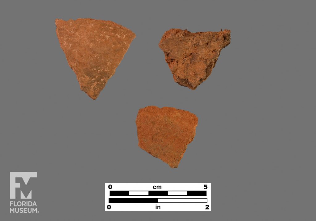 Formal artifact photo of three small red-colored sherds.