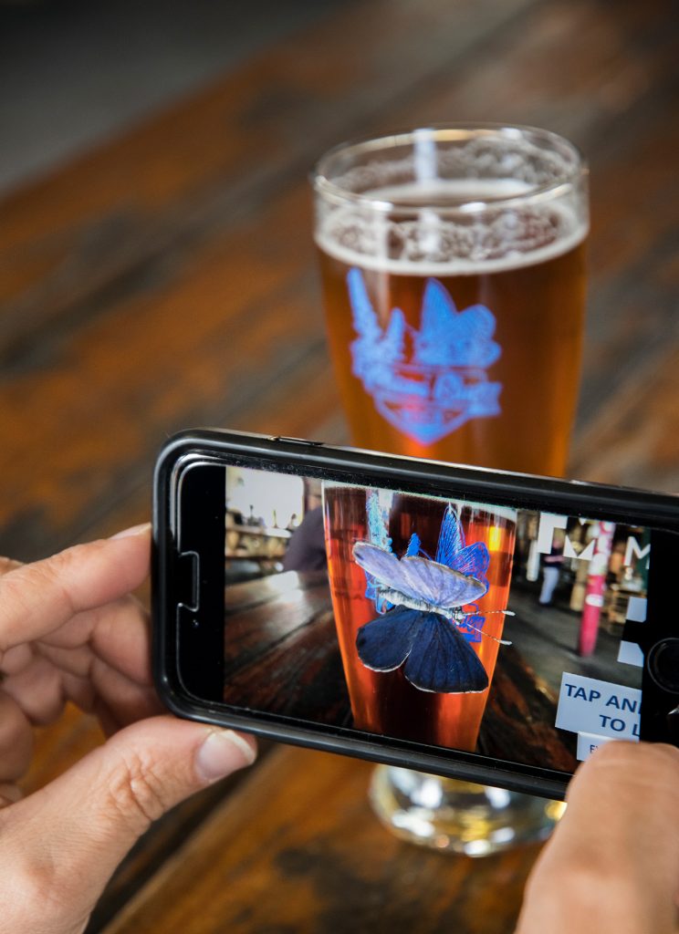 Close-up of a phone showing a beer glass with an augmented reality butterfly on a beer glass