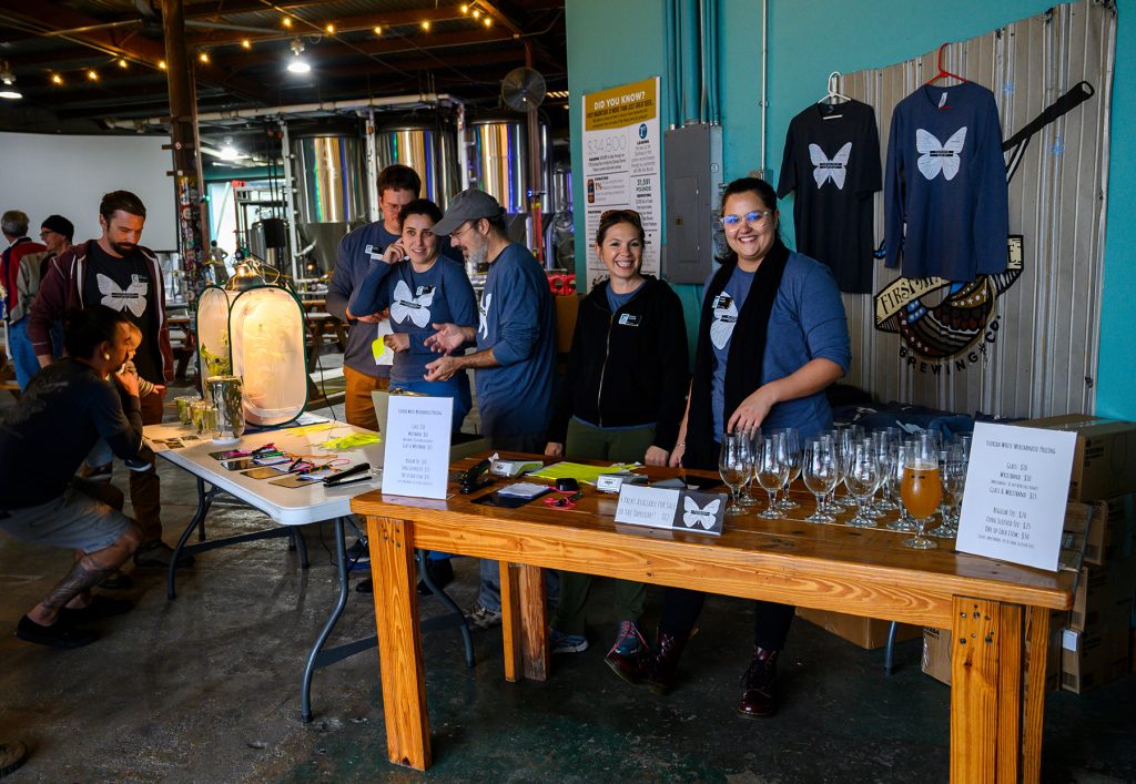 people wearing the Florida whit T-shirt stand behind tables filled with beer glasses and other merchandise