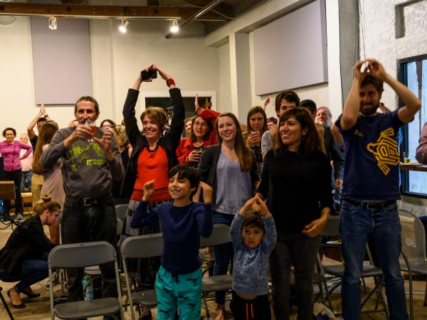 standing audience with some people using their hands to make the shape of shark fins on their heads