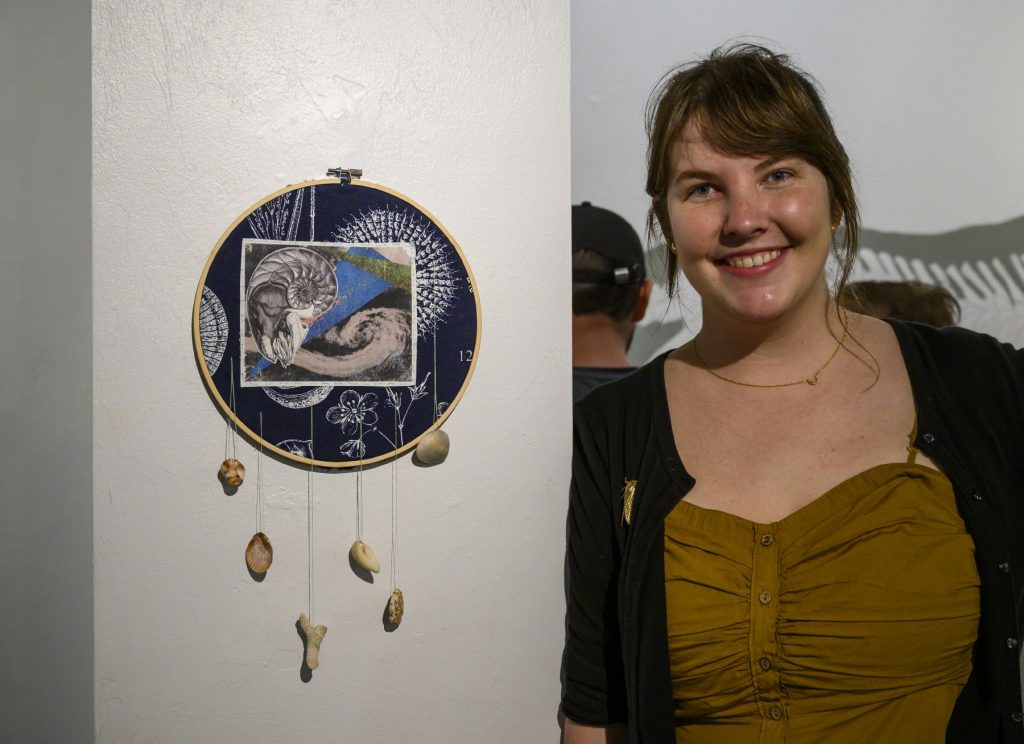 young artists stands next to her creation on the wall at an art gallery