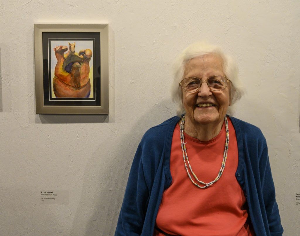 older lady standing next to a small painting in a gallery