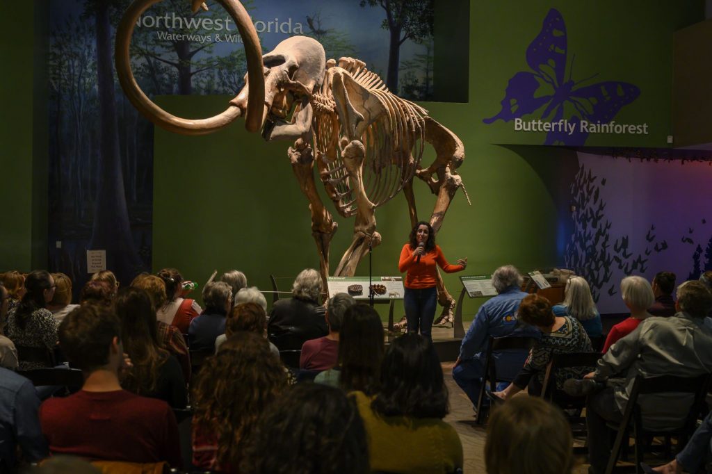 Sarah Steele Cabrera stands in front of mammoth skeleton and speaks to the audience