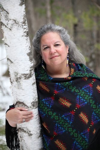 person standing leaning on a tree with a colorful wrap on