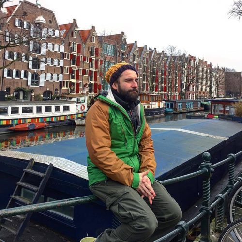 person sitting on rail, canal and river boats in background