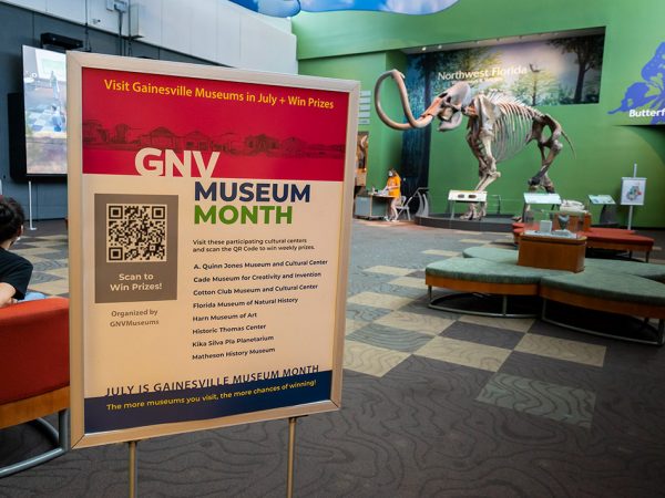 sign promoting GNV Museum Month in front of a museum gallery space with a fossil mammoth skeleton in the background