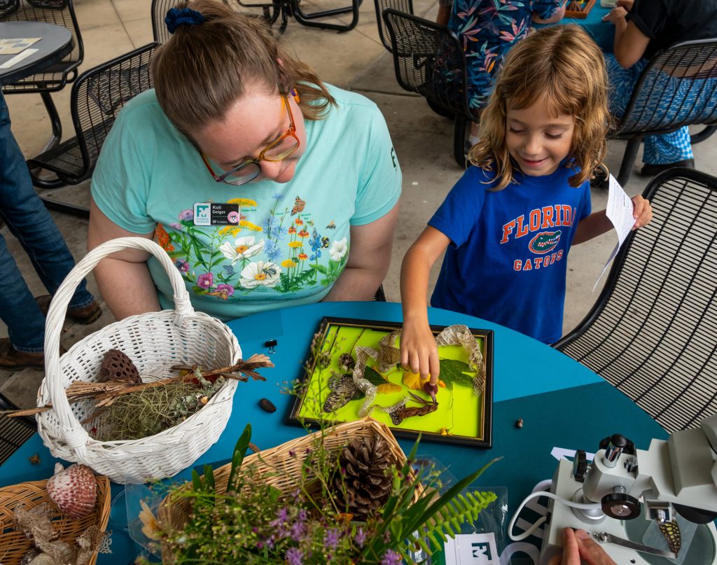 young child arranges plants collected and spread out of a table while museum worker watches