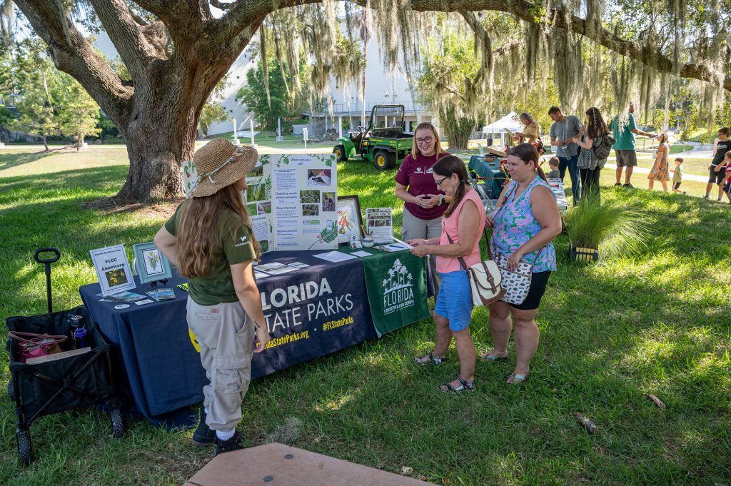 guests explore the Florida State park and other display tables under a large oak tree behind the museum