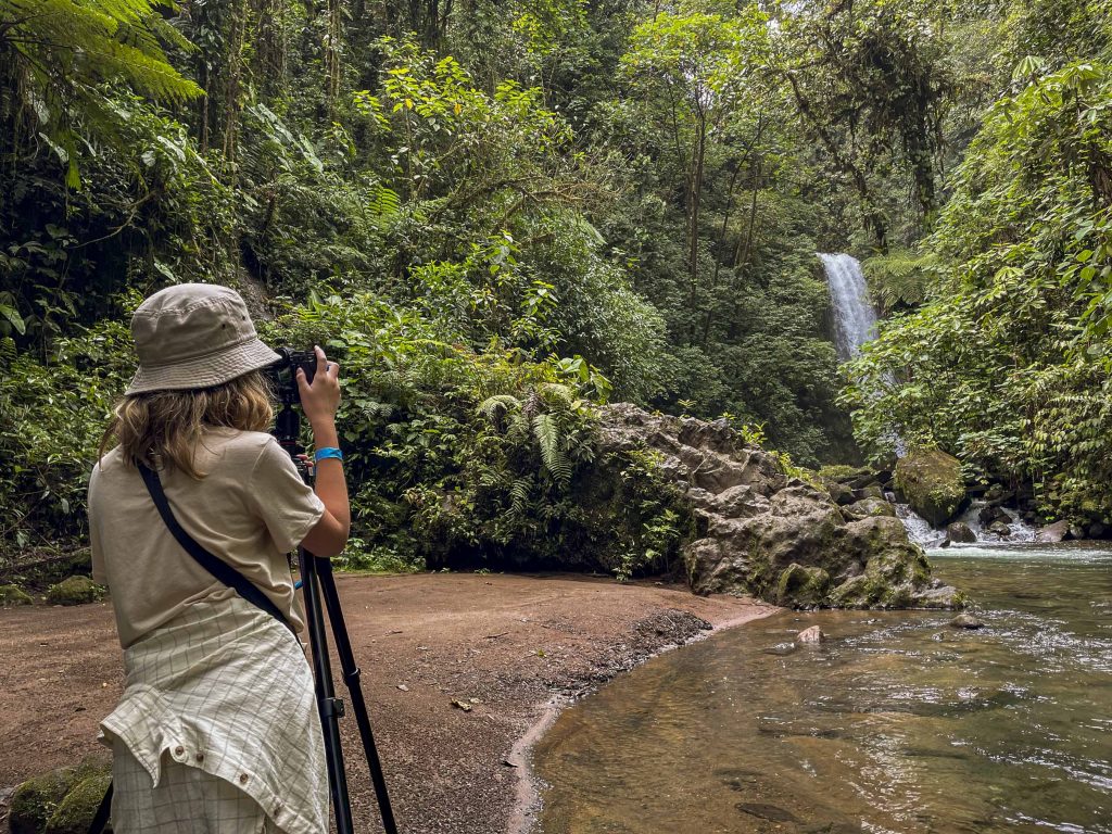A person uses a camera on a tripod to take a photograph of a waterfall.