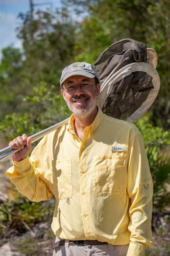 man in a yellow shirt holding a large butterfly net and smiling at the camera