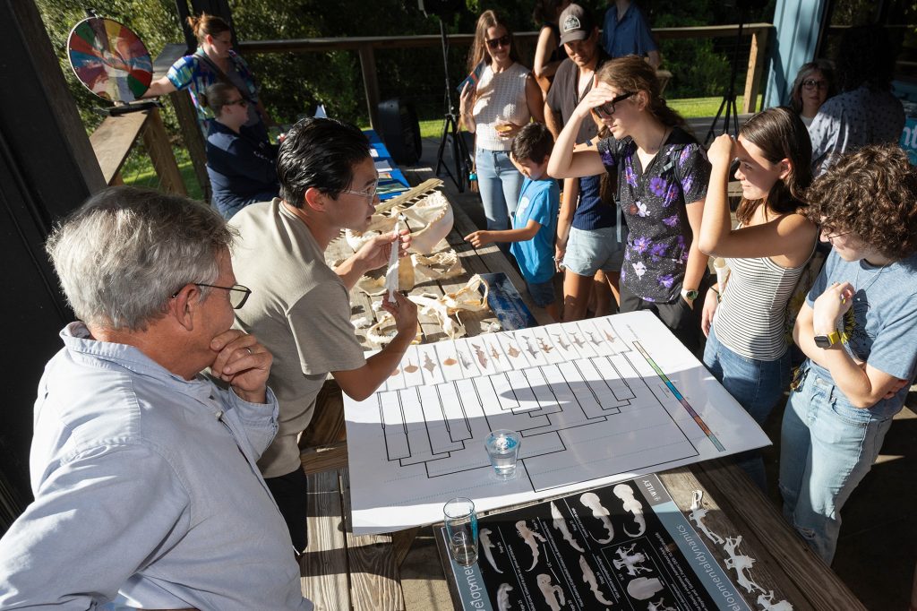 Two man seated at a table before posters about sharks and speak to a group of people