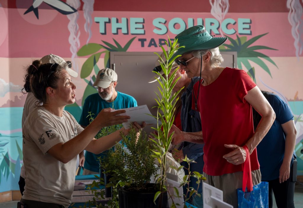 Daniels Lab researchers handing paper with information about the native plants to a visitor at Pollinator Palooza