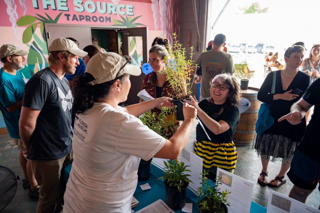 Daniels Lab researcher hands a plant to a woman in a bumble bee costume