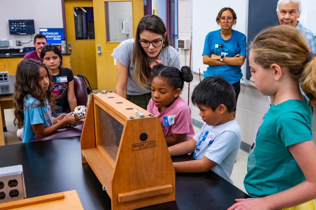 Kaitlin Deutsch and kids look at bees in an observation bee hive on display for the Family Discovery Camp Bees.
