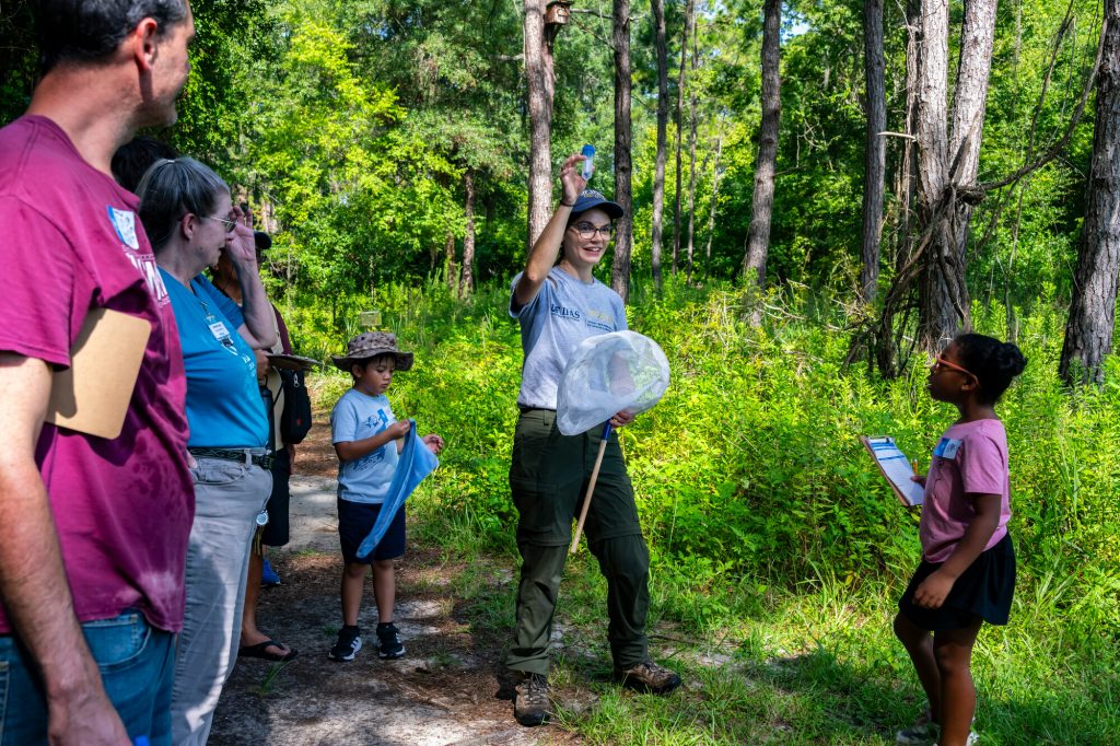 Kaitlin Deutsch holds up a collection tube and speaks to group of children and adults
