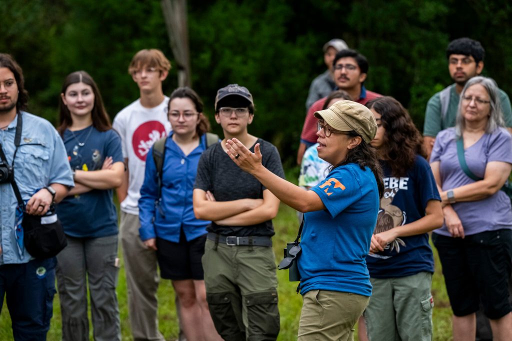 Glaucia Del-Rio speaks to event participants and they stand outside in a field