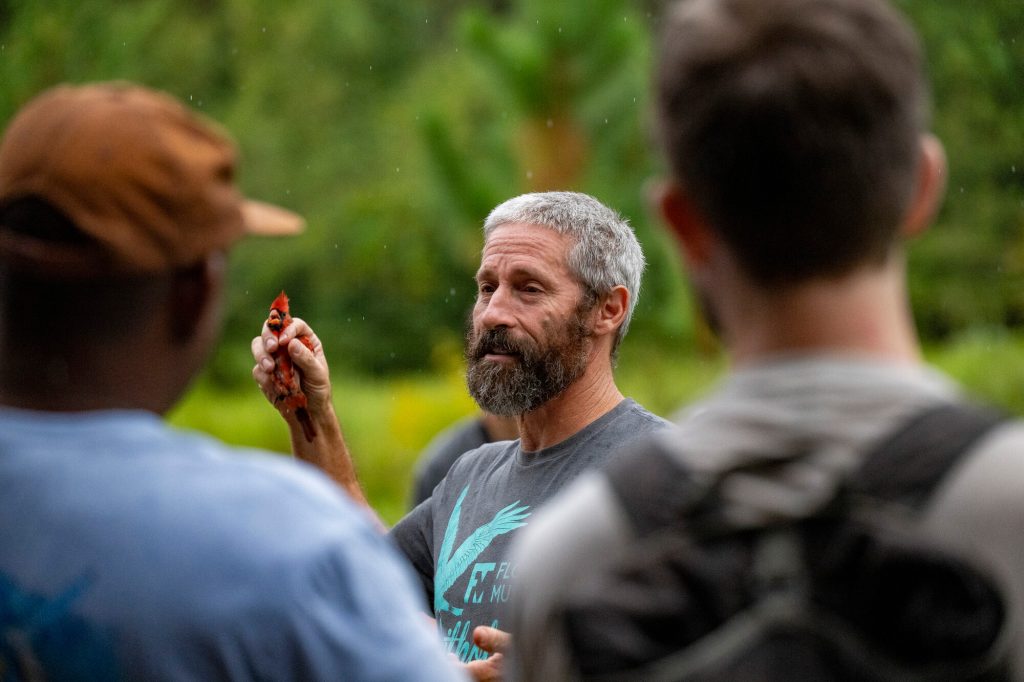 Charlie Muise holding a captured bird and speaking to participants observers in the Early Bird Gets the Band event