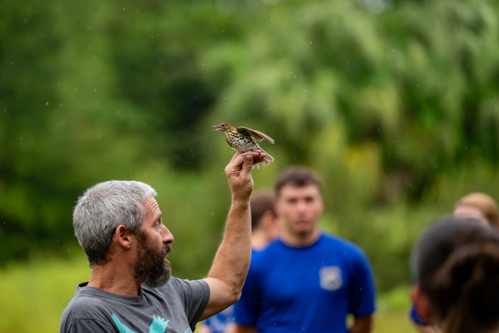 Charlie Muise holding a captured bird and speaking to participants observers in the Early Bird Gets the Band event