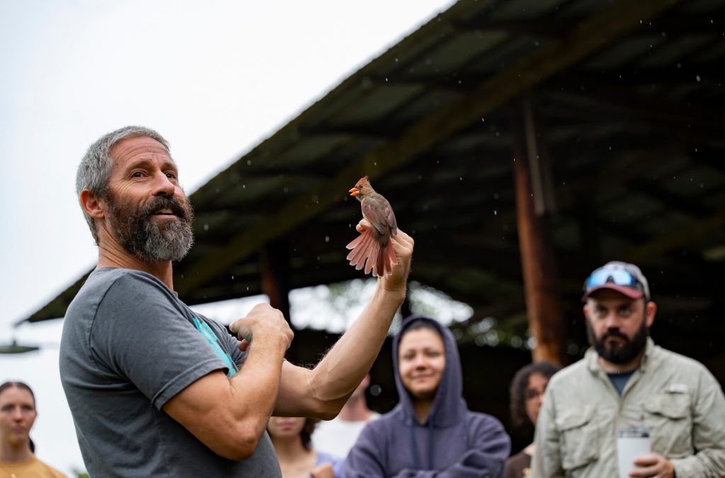 Charlie Muise holding a captured bird and speaking to participants observers in the Early Bird Gets the Band event