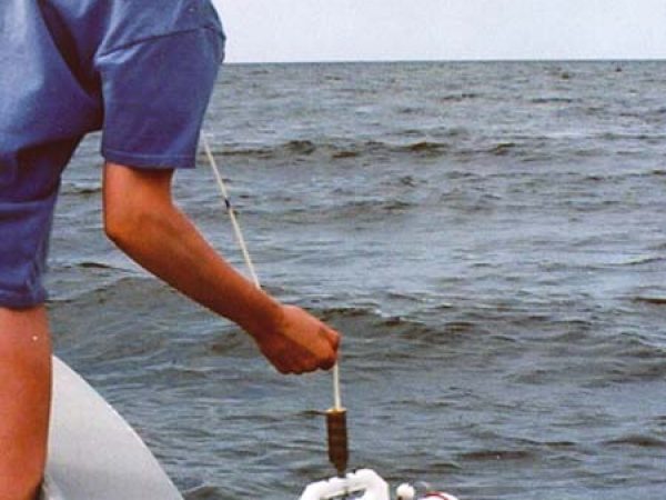 person lowering scientific equipment over the side of a boat
