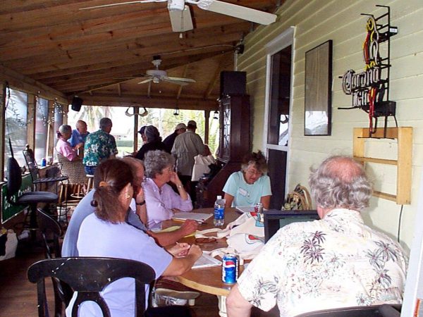 group of people sitting at tables set up on a covered porch