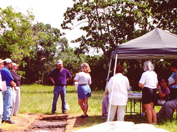 group of researchers standing in a field, some under a tent listening to one of the researchers speak