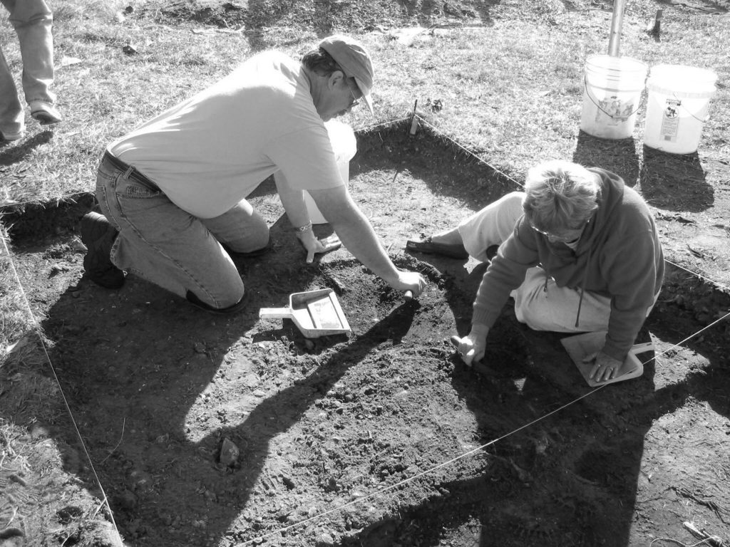 two people sitting and digging in shallow excavation pit