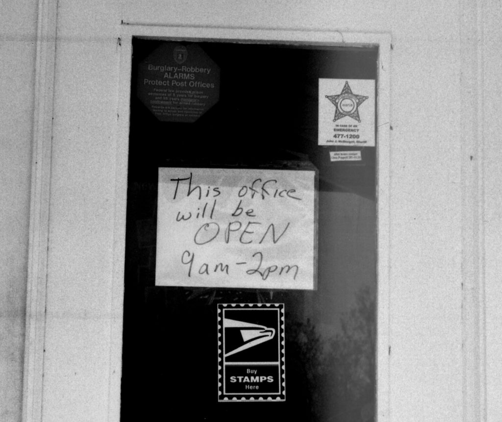 hand written sign on post office door reads This office will be OPEN 9am - 2pm